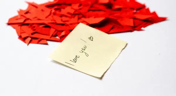 Serce z czerwonych skrawków papieru, a na nim karteczka z napisem "I love you!". Kocham Cię po polsku.