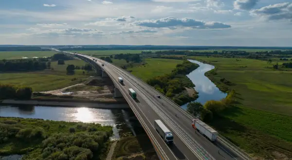 Most na Via Baltica przecina malowniczą dolinę rzeki, po której płyną ciężarówki.