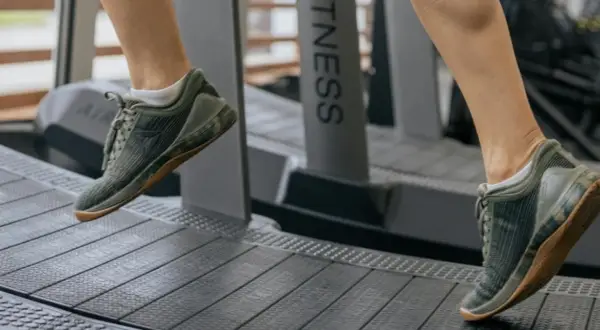 Dobre buty na bieżnię to klucz do komfortowego treningu. Na zdjęciu widać nogi w zielonych, sportowych butach na bieżni.