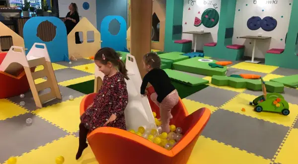 Dwie dziewczynki bawią się w sali zabaw Smart Kids Planet Warszawa. Jedna zjeżdża po zjeżdżalni do basenu z piłeczkami.