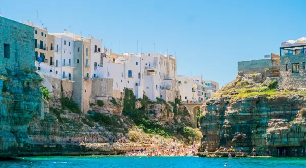 La famosa spiaggia di Polignano a Mare, con case bianche aggrappate alle scogliere e bagnanti che si godono il mare cristallino.