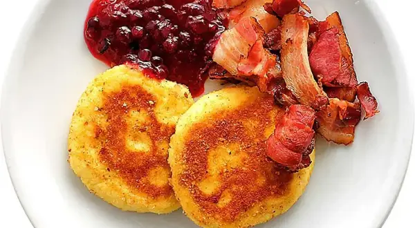 Två gyllene potatisbullar med knaperstekt bacon och rårörda lingon. Ett klassiskt potatisbullar recept som passar perfekt till helgfrukosten.