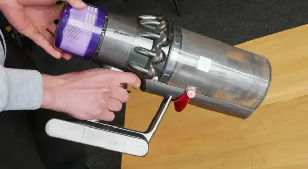 Ręce demontują fioletowy filtr z odkurzacza Dyson, przygotowując go do czyszczenia filtra magnetycznego.