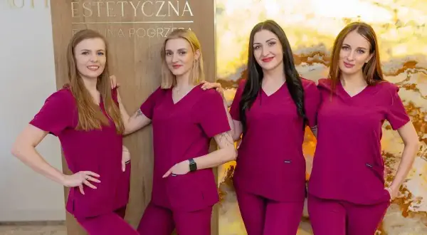 Cztery kobiety w uniformach medycznych stoją obok siebie przed tablicą z napisem "Kosmetologia Estetyczna".