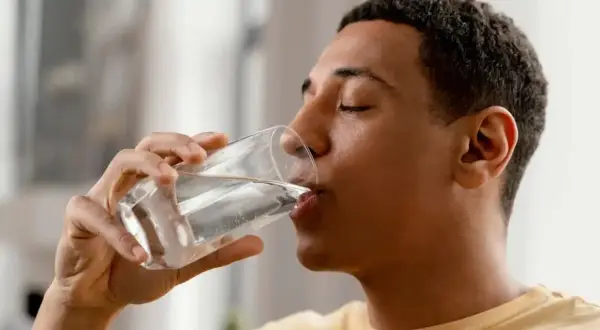 Un jeune homme boit un verre d'eau minérale magnésium, une boisson rafraîchissante et bénéfique.