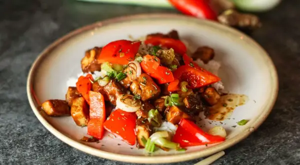 Leckeres, klebriges Tofu-Rezept mit Reis, Paprika und Frühlingszwiebeln, garniert mit Kräutern.
