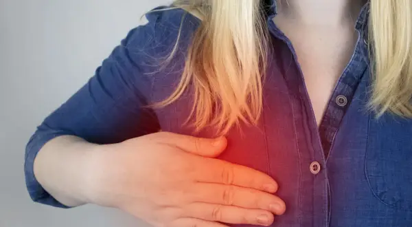 Kobieta z blond włosami dotyka piersi, gdzie widoczny jest czerwony obszar bólu, sugerujący potrzebę biopsji torbieli w piersiach.