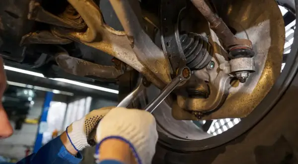 Mechanik dokręca śrubę w zawieszeniu samochodu kluczem.