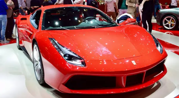 Błyszczący, czerwony Ferrari 488 GTB na wystawie, otoczony ludźmi podziwiającymi jego sportowy design.