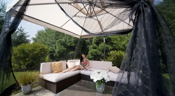 Kobieta relaksuje się na sofie pod dużym parasolem, który chroni przed słońcem i owadami. Idealny parasol na balkon.