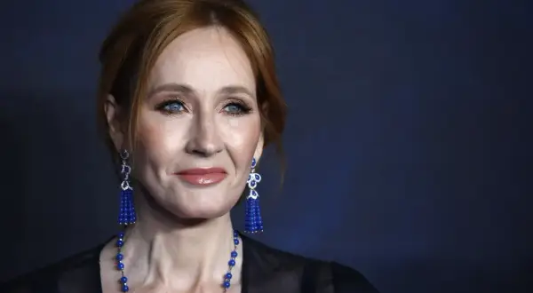 Portret J.K. Rowling z rudymi włosami, niebieskimi oczami i wiszącymi kolczykami.