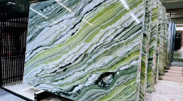 Lastre di marmo verde di prato con venature bianche e nere, esposte in un magazzino.