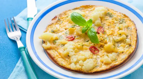 Omlet z kalafiorem i pomidorkami, idealny na lekki obiad. Udekorowany listkiem bazylii.