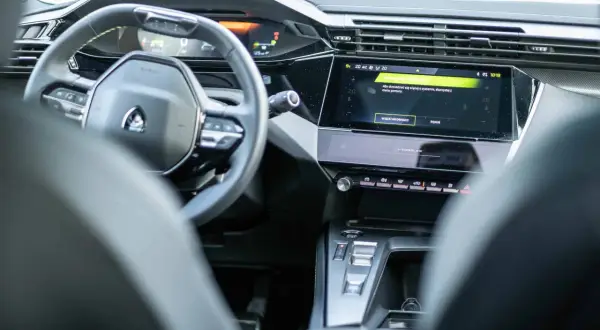 Nowoczesne wnętrze Peugeot 408 z cyfrowymi zegarami i ekranem dotykowym. Widoczny fragment kierownicy i konsoli środkowej.