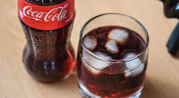 Szklanka z lodem i napojem, obok butelka Coca-Coli. Czerwone wino z colą w szklance, orzeźwiające.