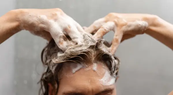 Manos con espuma masajean el cuero cabelludo, demostrando cómo lavarse el pelo correctamente para una limpieza profunda y un cabello saludable.