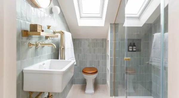 Elegantes mini aseos de cortesía con azulejos verde menta, lavabo blanco, ducha acristalada y luz cenital.