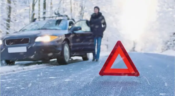 Gefährliche Straße: Ein Auto mit Warnblinker, eine Person und ein Warndreieck im Schnee. So entsteht Blitzeis.