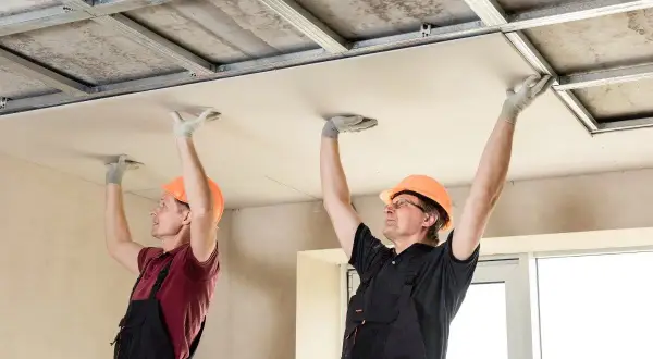 Deux ouvriers en casque orange installent des plaques de plafond, une étape clé de la rénovation plafond.