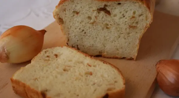 Pyszny chleb cebulowy na drożdżach, świeżo upieczony, z widocznymi kawałkami cebuli w miękiszu. Obok leżą całe cebule.