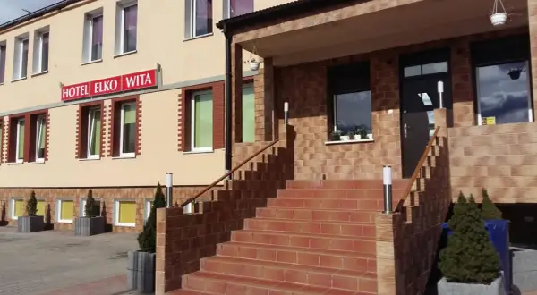 Wejście do hotelu Elko Elbląg. Schody prowadzą do drzwi, a nad nimi widnieje czerwony szyld.