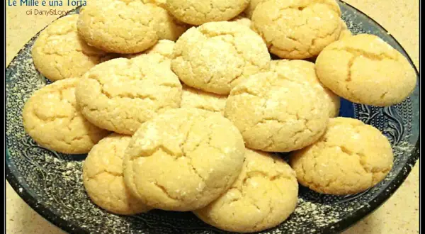 Biscotti con farina di mandorle, dorati e friabili, adagiati su un piatto scuro.