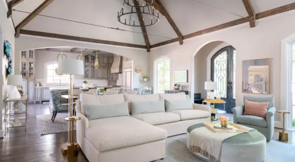 A spacious living room with a sectional sofa, armchair, and ottoman. The vaulted ceiling with exposed beams and a large chandelier create a dramatic focal point, showcasing what is the best way to arrange furniture for an open, airy feel.