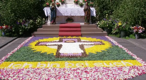 Blumenbild mit Kreuz und Schriftzug "Ich bin das Licht der Welt" vor einem Altar. Ein Fest für Fronleichnam.