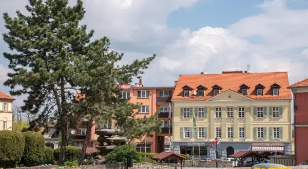Rynek w Sobótce z kamienną rzeźbą i żółtym budynkiem.