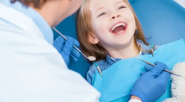 Uśmiechnięta dziewczynka u dentysty, która ma krzywy zgryz. Lekarz bada jej zęby.