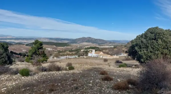 Paisaje de la sierra maria con una iglesia blanca y un campanario, rodeada de vegetación y montañas al fondo.