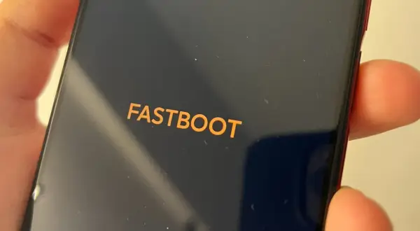 Pomarańczowy napis FASTBOOT na ciemnym ekranie telefonu, trzymanego w dłoni.