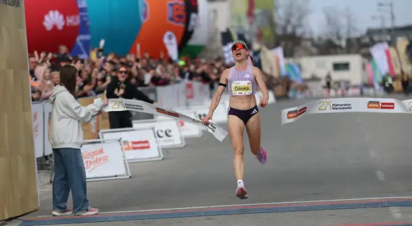 Radość na mecie Półmaratonu Warszawskiego 2026. Zawodniczka Glinka przekracza linię mety, a tłum wiwatuje.