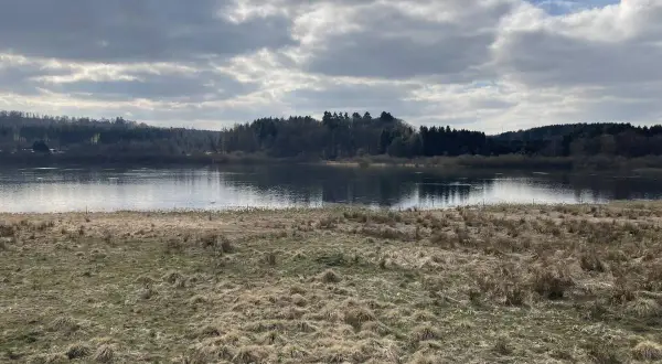 Ein ruhiger Blick auf den Krombachtalsperre Rundweg mit bewaldeten Ufern und einem Himmel voller Wolken.