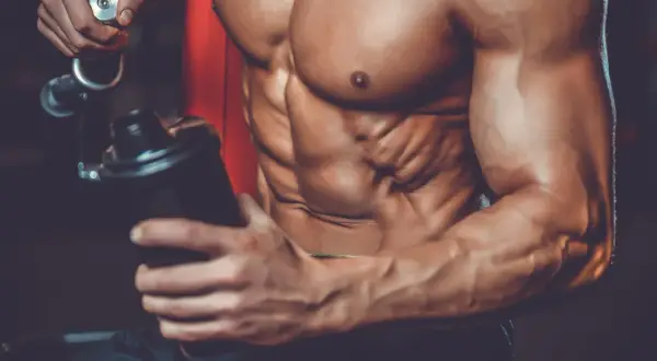Atleta con addominali scolpiti prepara un frullato, mostrando a cosa servono le proteine in polvere palestra per la crescita muscolare.