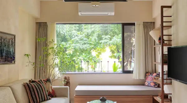 Cozy living room with a large window overlooking lush greenery, a comfortable sofa, and a built-in bench, making this small house feel spacious.