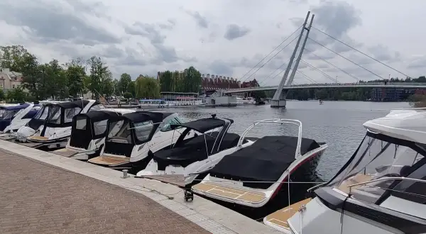 Łodzie zacumowane w porcie, z mostem w tle. Idealne miejsce, by zacząć planować, jak dojechać do Mikołajek i cieszyć się Mazurami.