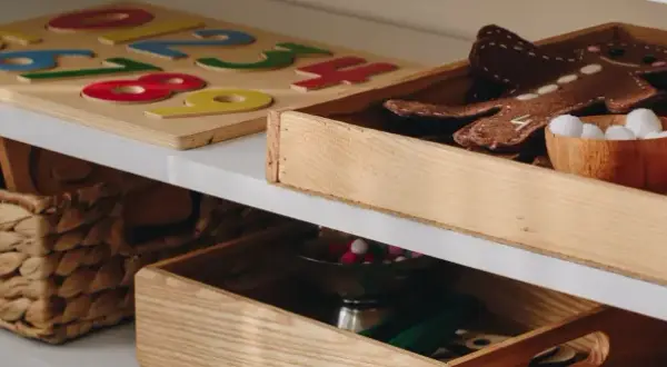 Drewniane pudło na zabawki z pluszowym piernikiem i kuleczkami. Obok puzzle z cyframi i wiklinowy kosz.