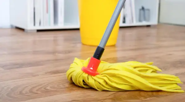 Ein gelber Wischmopp liegt auf einem Holzfußboden, bereit, den Boden zu wischen. Ein gelber Eimer steht im Hintergrund.