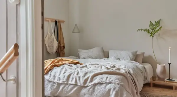 Sovrum med en bäddad säng i olika nyanser av beige. En gul filt ligger överst. Frågan "hur blandar man beige" besvaras här med en lugn och harmonisk inredning.