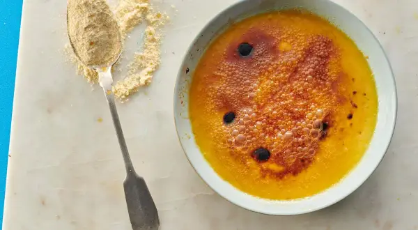 Ein Löffel mit feinem Puder liegt neben einer Schüssel mit karamellisiertem Creme Brulee.