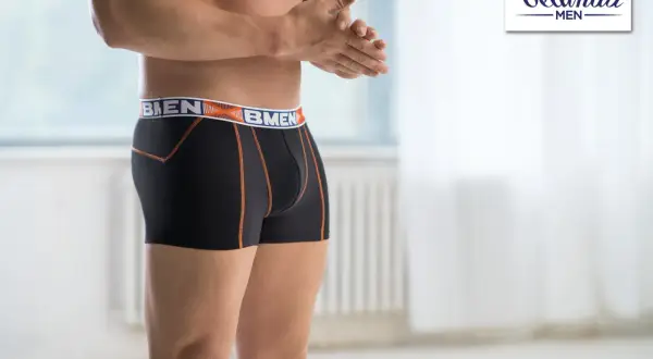 Mężczyzna w czarnych bokserkach z pomarańczowymi szwami i logo marki. Wybór między slipami a bokserkami to kwestia komfortu.