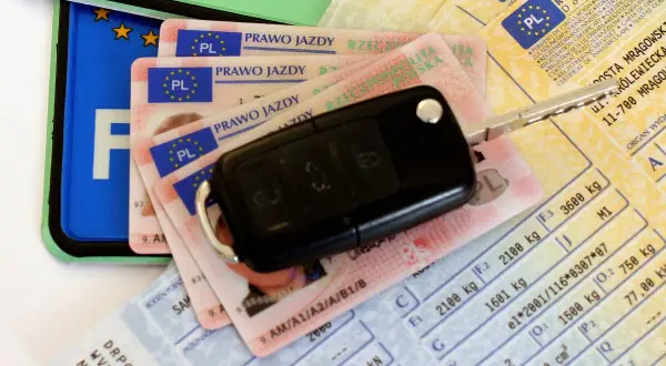 Kluczyki do auta i dokumenty, w tym prawo jazdy. Czy prawo jazdy jest bezterminowe? Na zdjęciu widać też dowód rejestracyjny i tablicę.