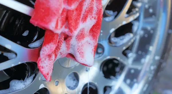 Un chiffon rouge savonneux nettoie une jante de voiture brillante. Un nettoyant jantes maison efficace pour un résultat impeccable.