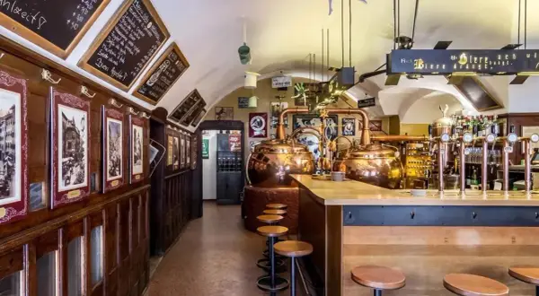 Interno di un locale tradizionale con alambicchi di rame, sgabelli e insegne che richiamano il mondo della birra e del **hopfen & co.**