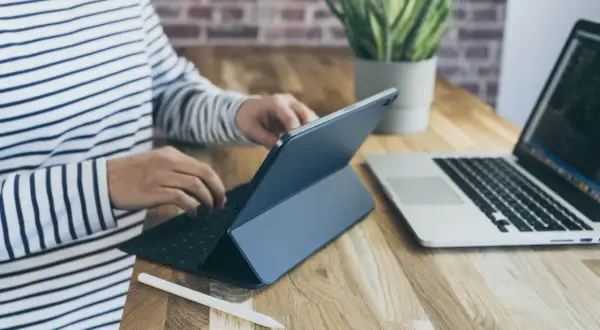 Osoba w paski pracuje na tablecie z klawiaturą, obok laptop. Może sprawdzać kursy walut w getin bank.