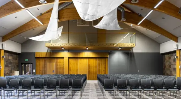 Nowoczesna sala konferencyjna z rzędami czarnych krzeseł, drewnianymi elementami i kamienną ścianą. Idealne miejsce na konferencje na Mazurach.