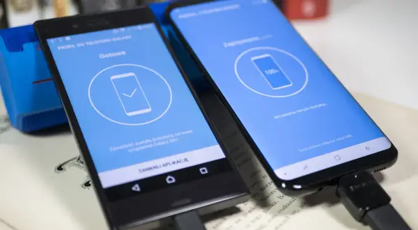 Dwa telefony połączone kablem USB, jeden wyświetla komunikat "Gotowe", drugi "100%", pokazując jak przenieść dane z telefonu na telefon Samsung.