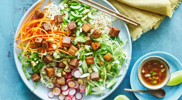 En färgglad asiatisk nudelsallad med krispiga grönsaker, cashewnötter och gyllene tofu-kuber. Serveras med en dressing och limeklyftor.