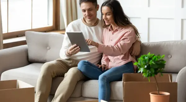 Couple sur un canapé, regardant une tablette. Des cartons de déménagement sont autour d'eux, peut-être pour une lettre pour quitter son logement sans préavis.